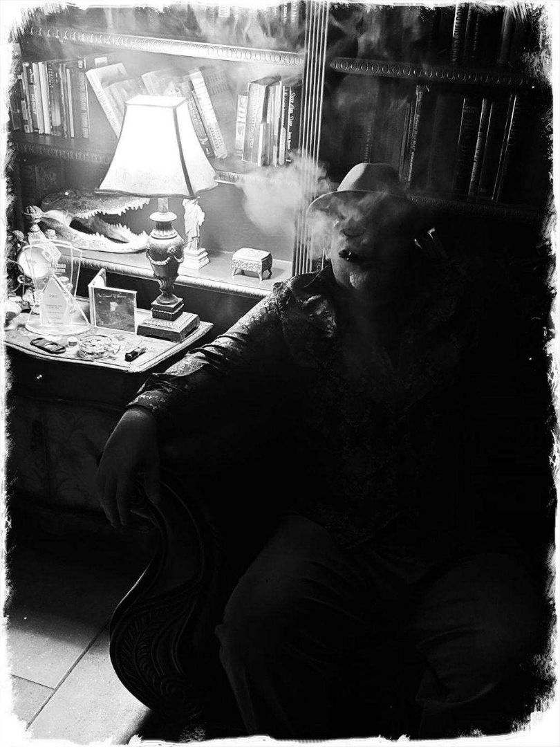 Uncle Ryano sitting in his library smoking a cigar in black and white.
