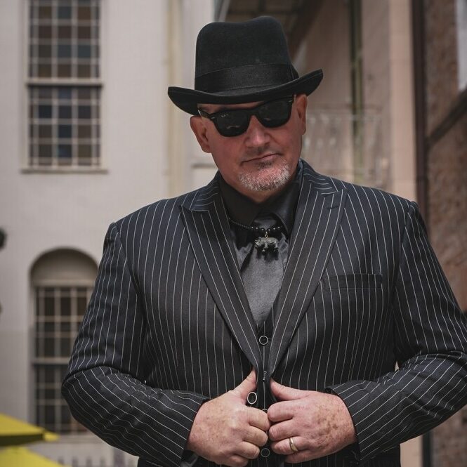 Uncle Ryano in Pin Stripe Suite in front of old building.